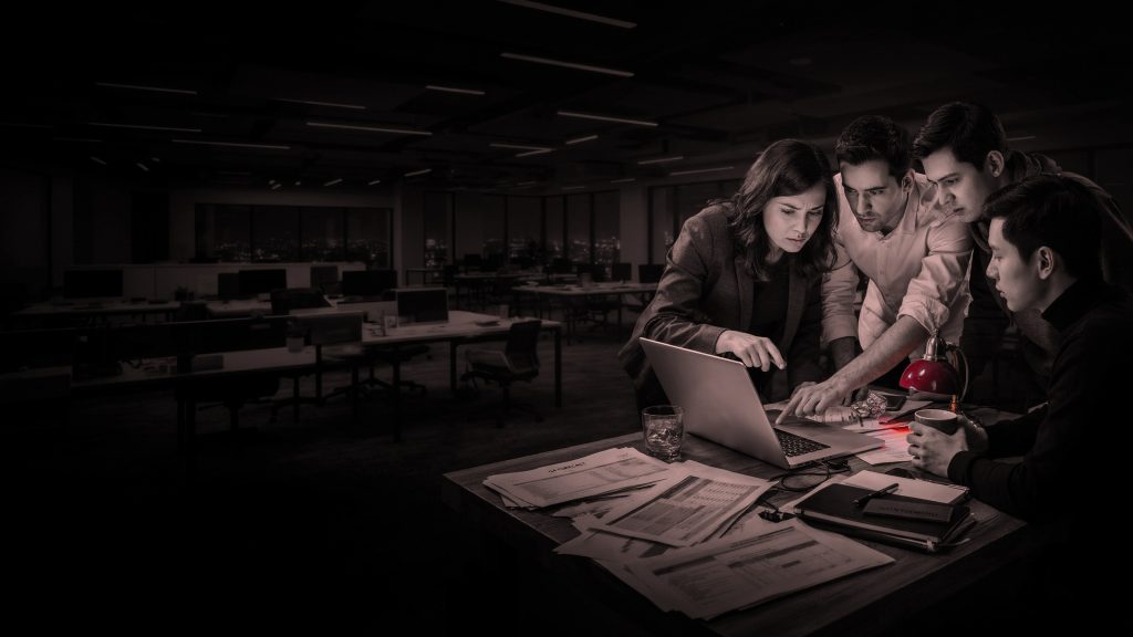 Colleagues in a dark office huddled round a laptop, lit red