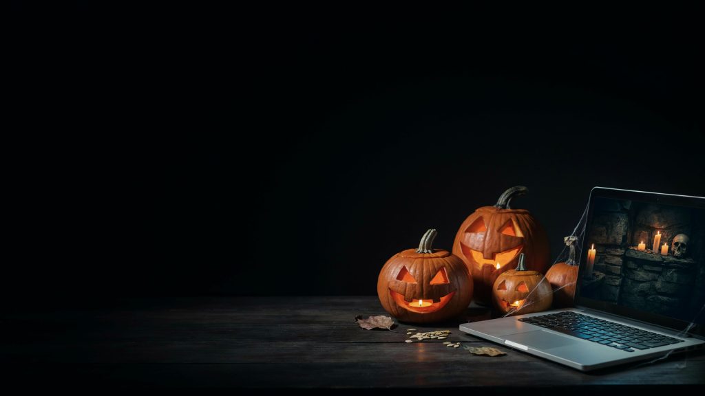 Glowing jack-o-lanterns beside a laptop showing a candle lit crypt